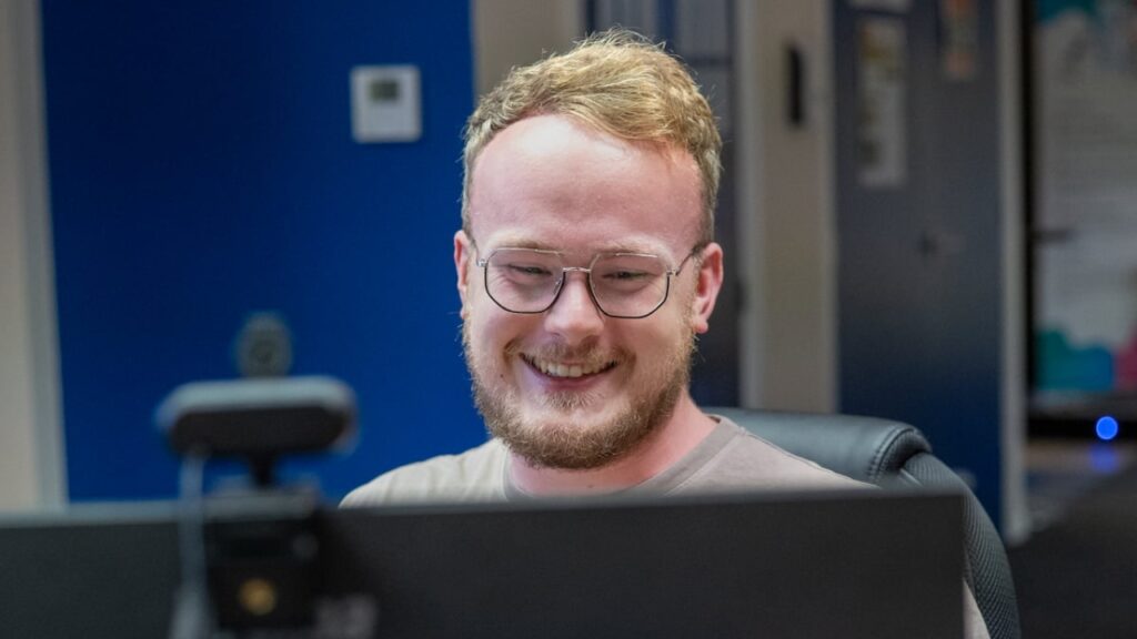 Man behind a computer smiling at screen