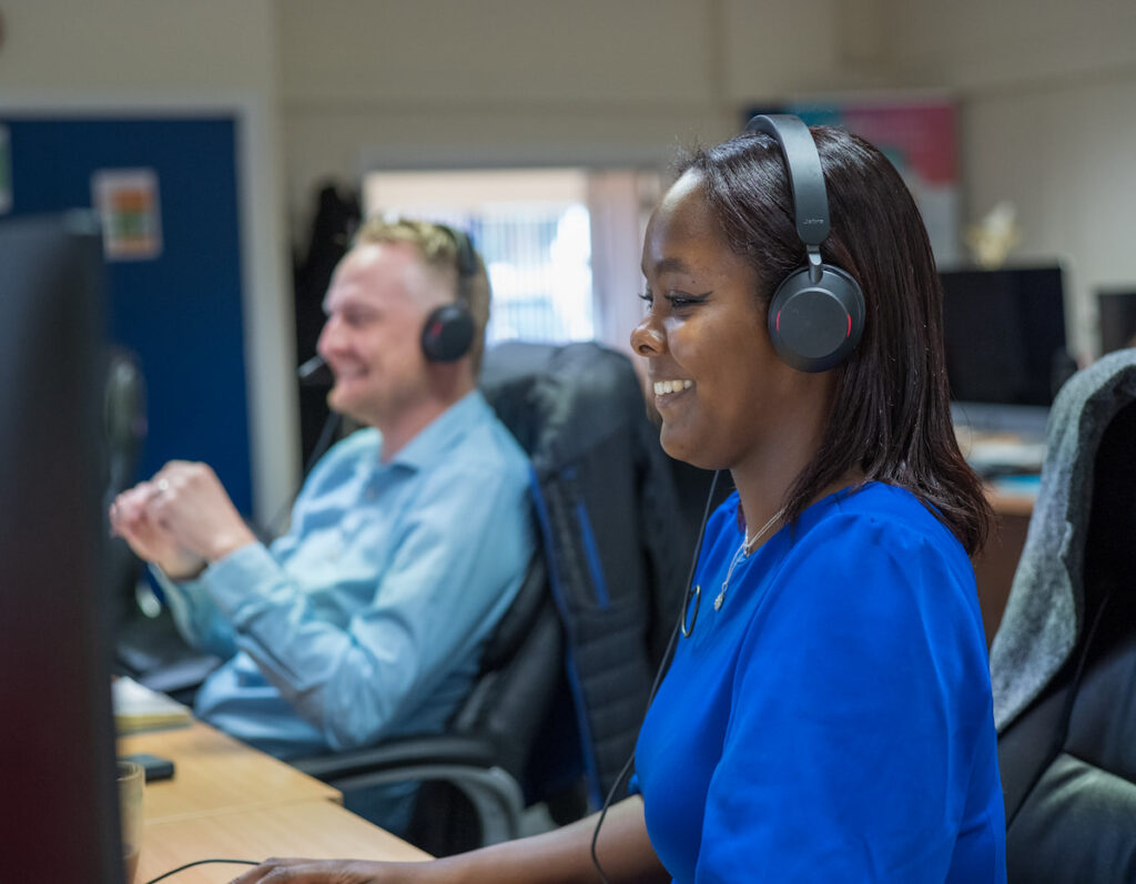 2 people smiling at computers with headsets on