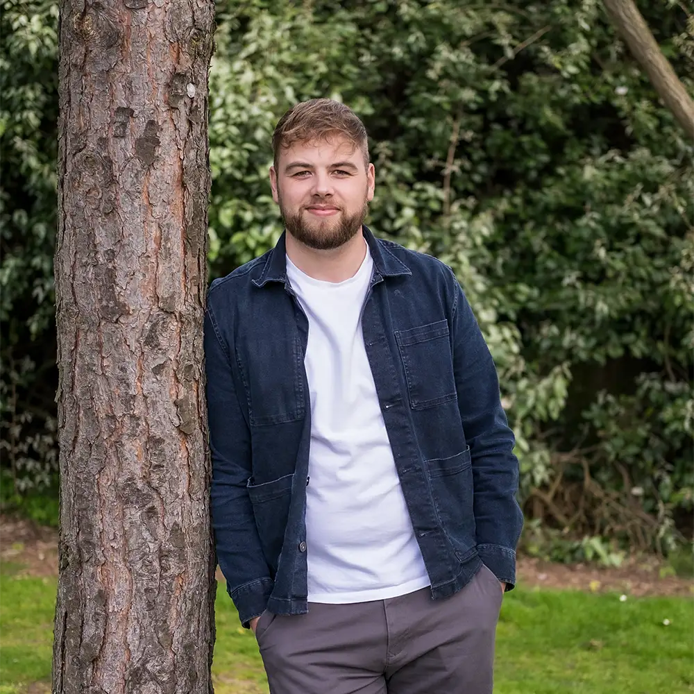 Man smiling at camera and leaning on tree