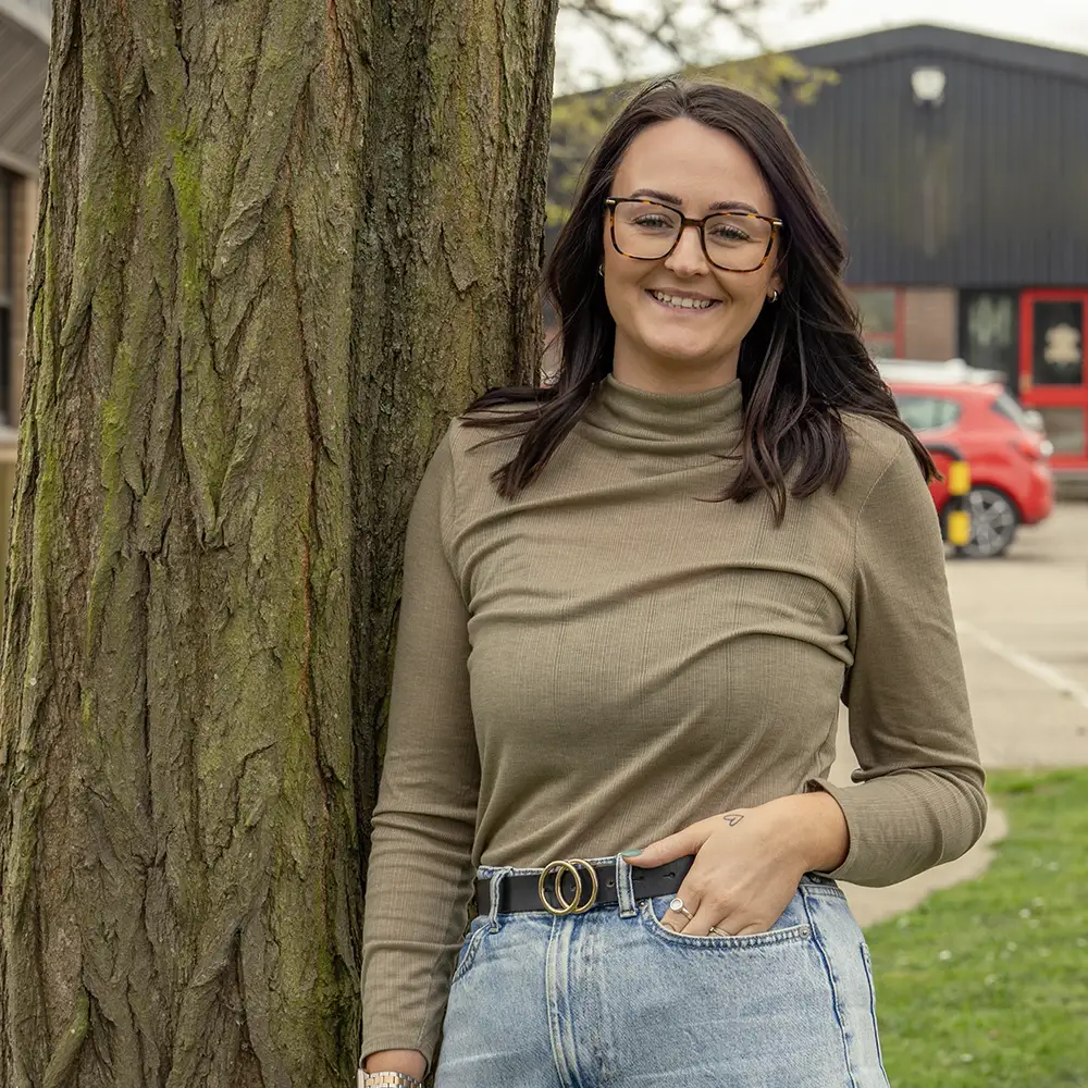 Zoe leaning against a tree smiling to camera