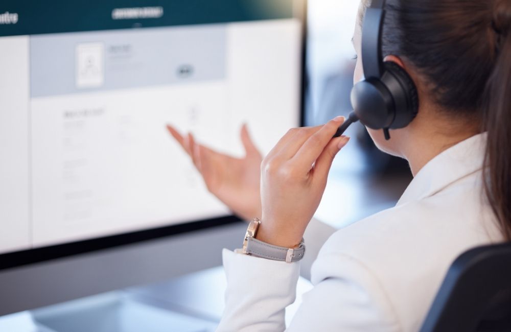 Woman wearing headset talking on phone, looking at a computer screen